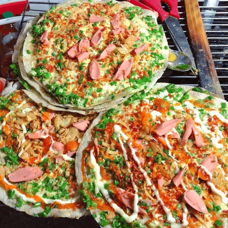 Banh trang nuong topped with egg, scallions, and sauces at a Ho Chi Minh street stall