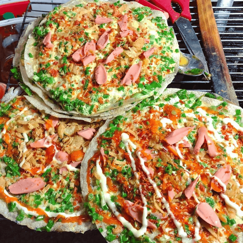 Banh trang nuong topped with egg, scallions, and sauces at a Ho Chi Minh City street stall