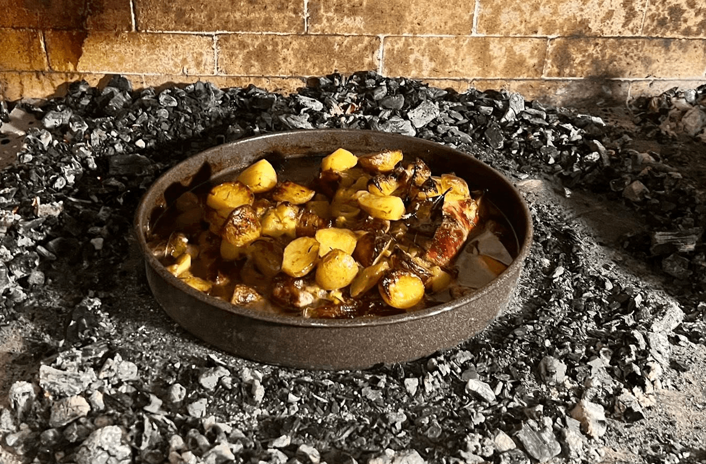 Peka roasting with potatoes in a pan over embers