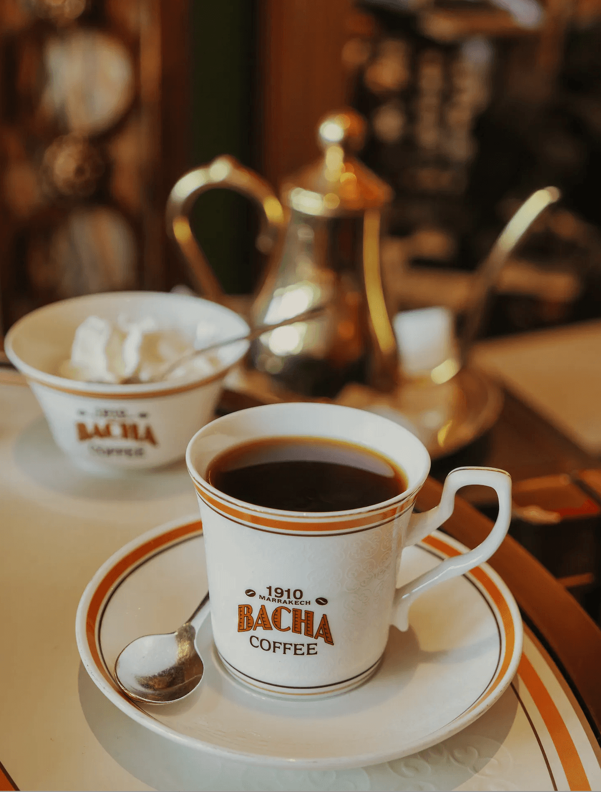 A cup of Bacha Coffee served in Marrakesh with silver coffee service in the background