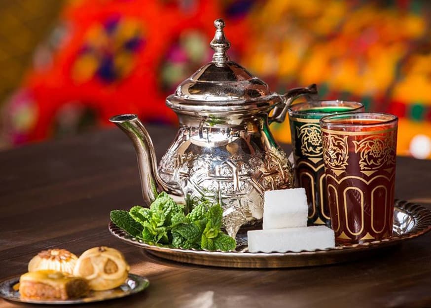 A traditional Moroccan mint tea service with a silver teapot, mint, sugar cubes, and tea glasses