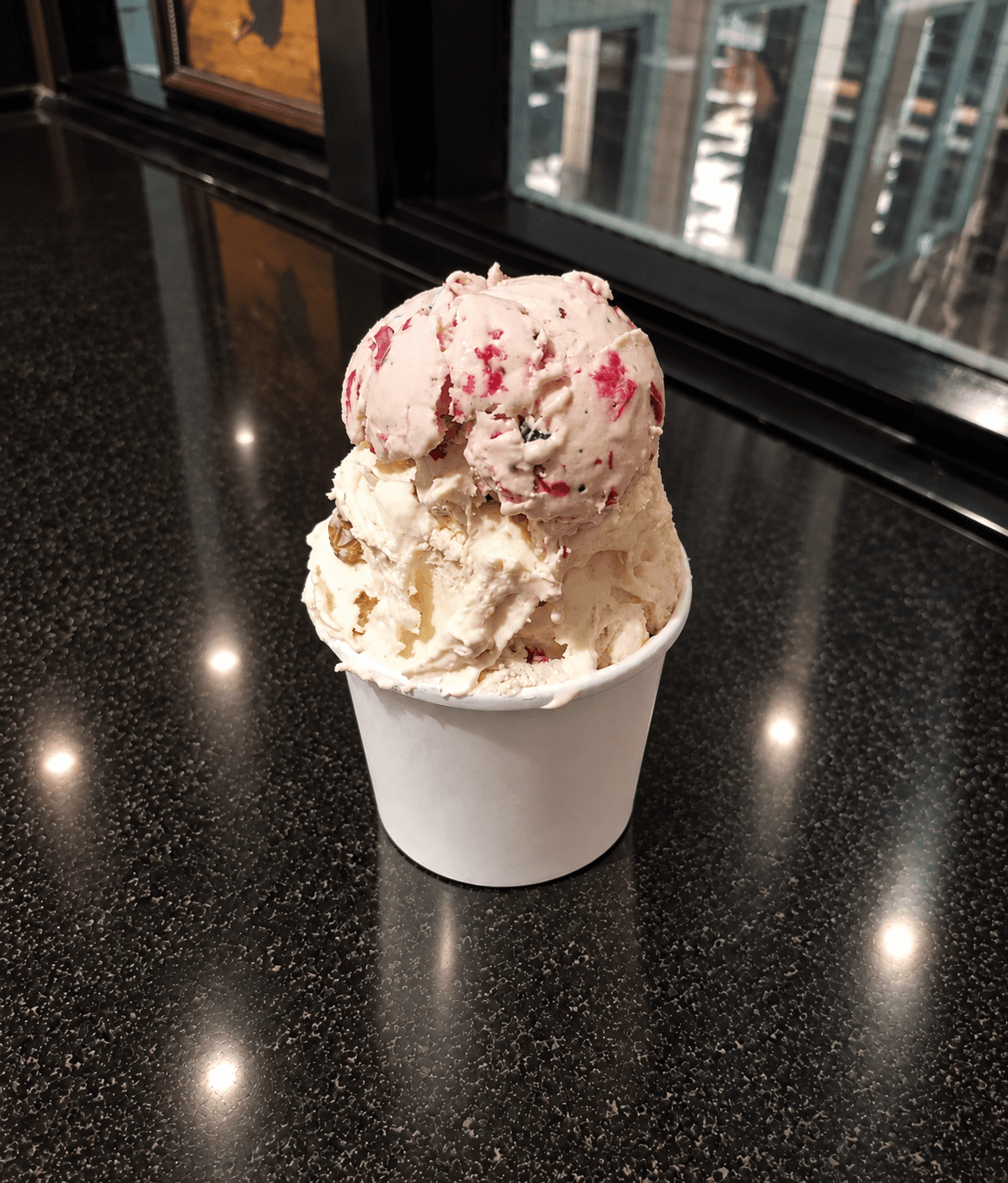 Three scoops of Arethusa Farm ice cream in a white paper cup on a glossy tabletop