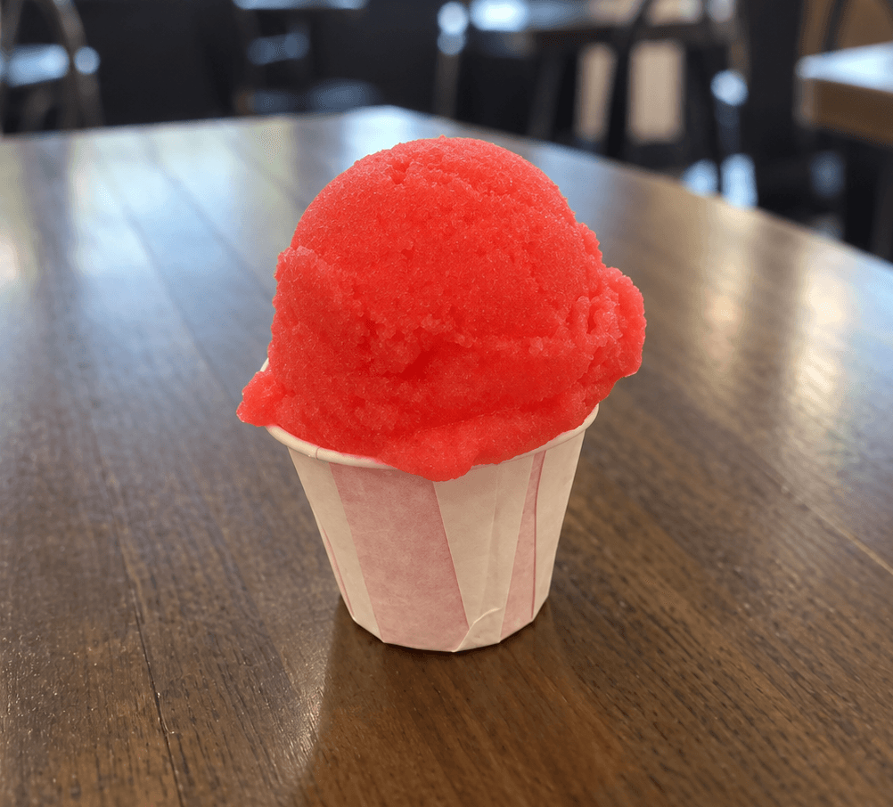 Bright red Italian ice in a small paper cup on a restaurant table