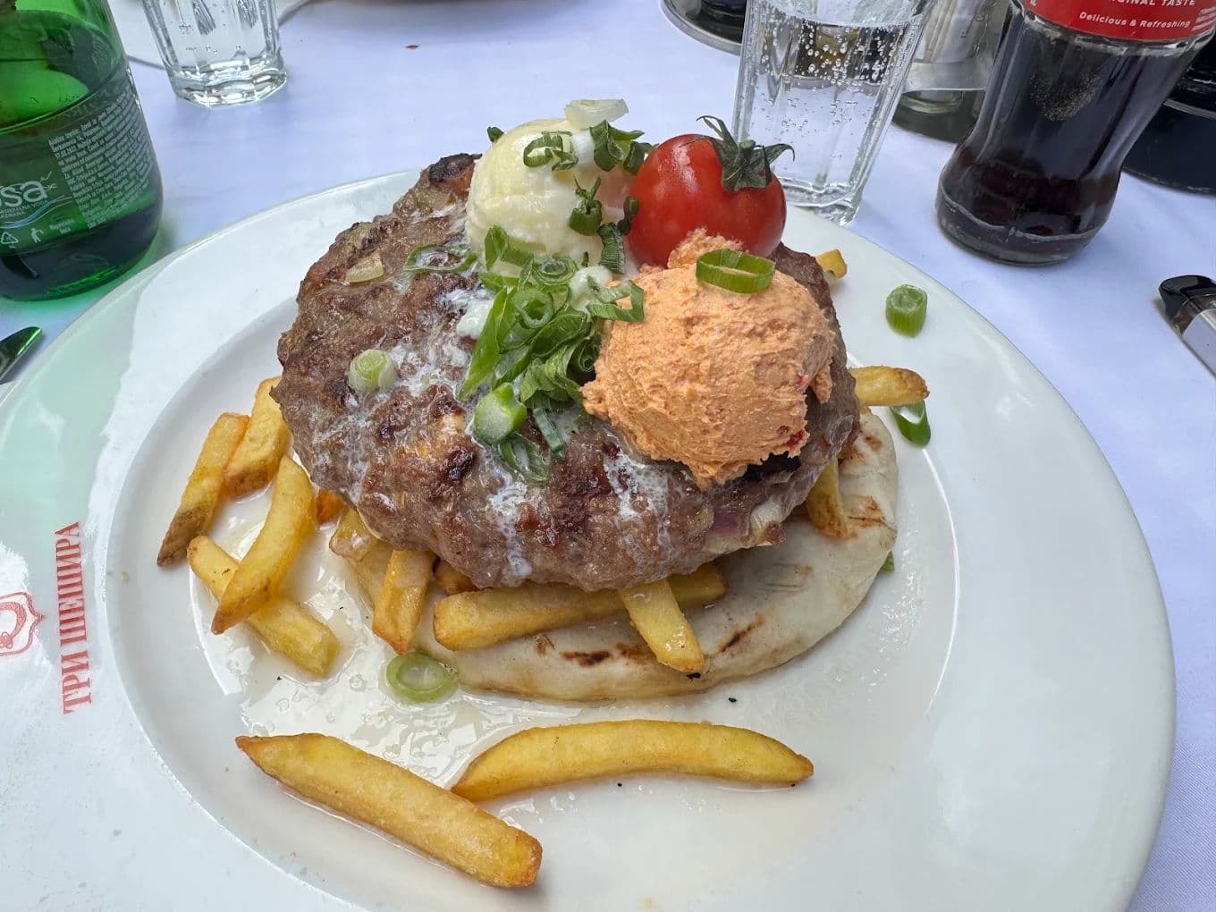 Pljeskavica served on flatbread with fries, kajmak, and a spicy spread