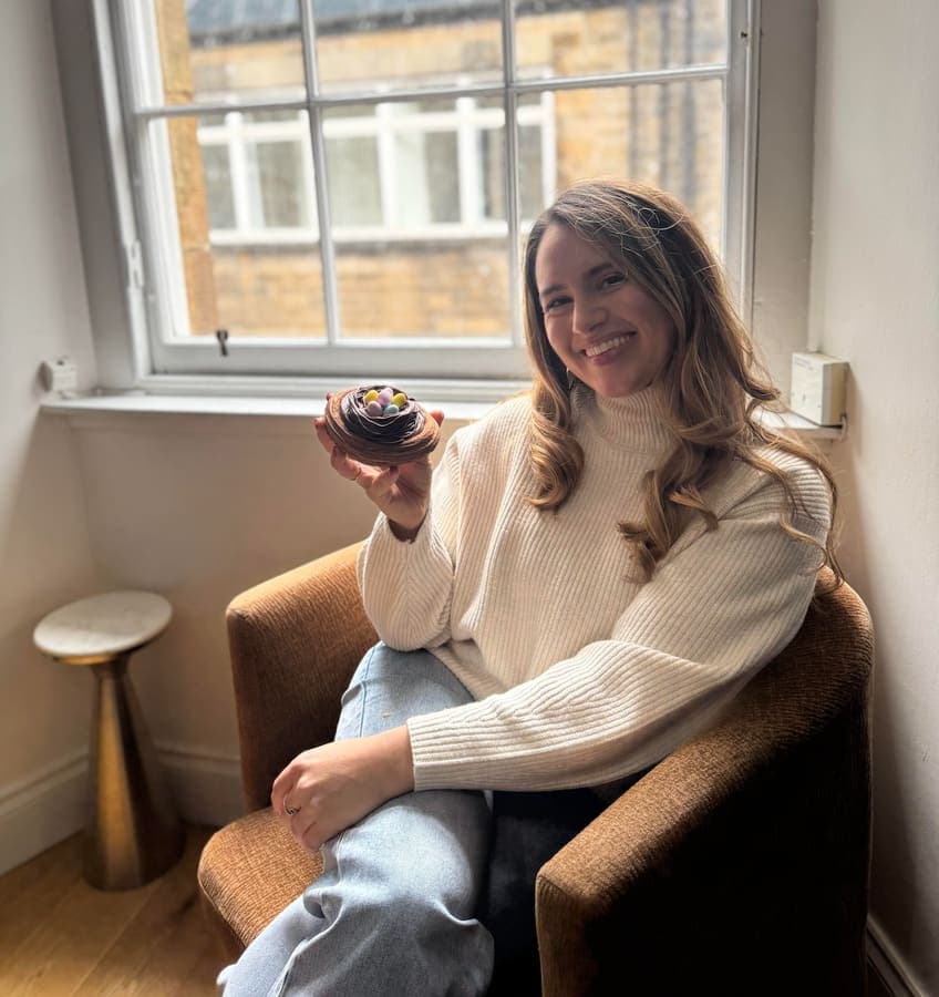 Sarah smiling with a small dessert by a window