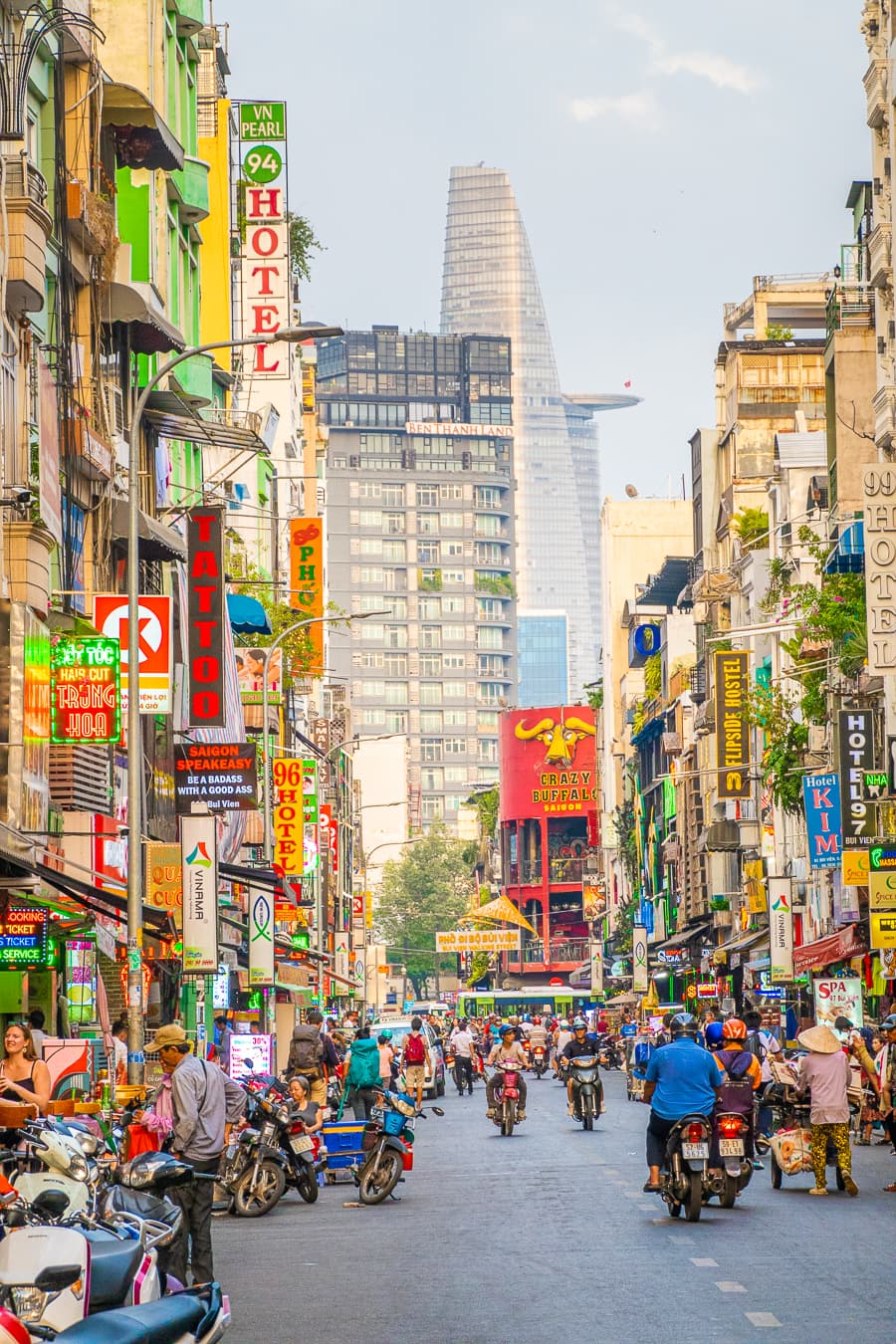 Busy Saigon street scene with motorbikes, neon signs, and the skyline rising in the background