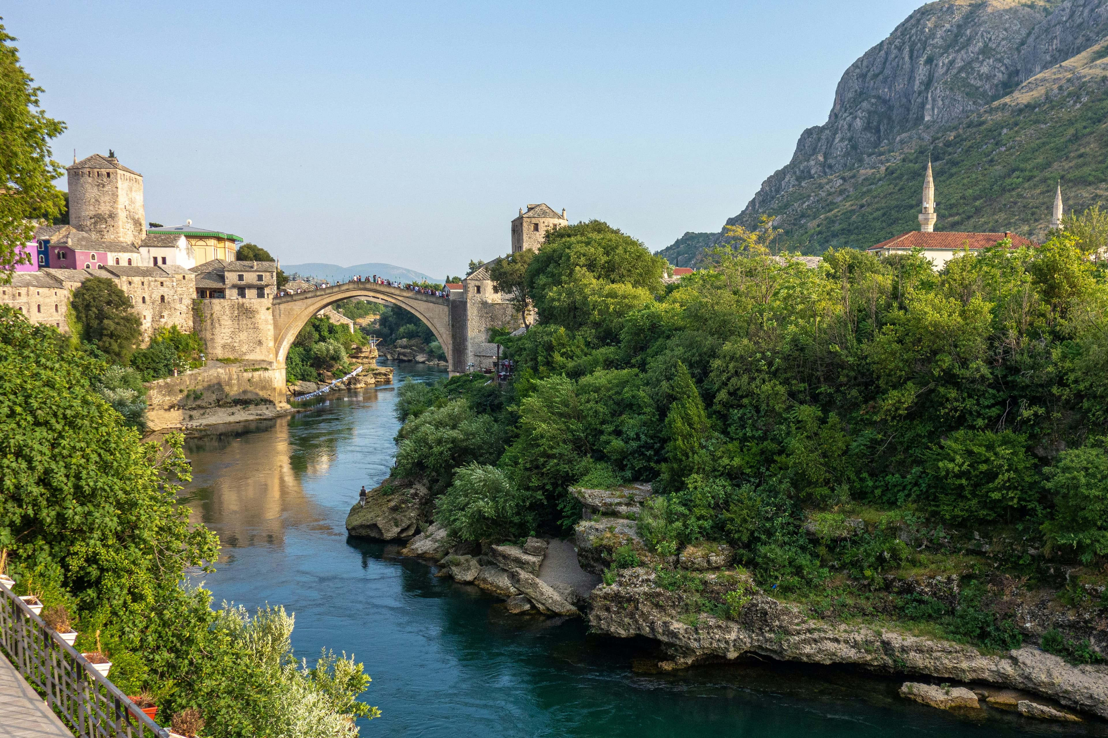 Mostar's Old Bridge over the Neretva River with stone towers and mountains behind it