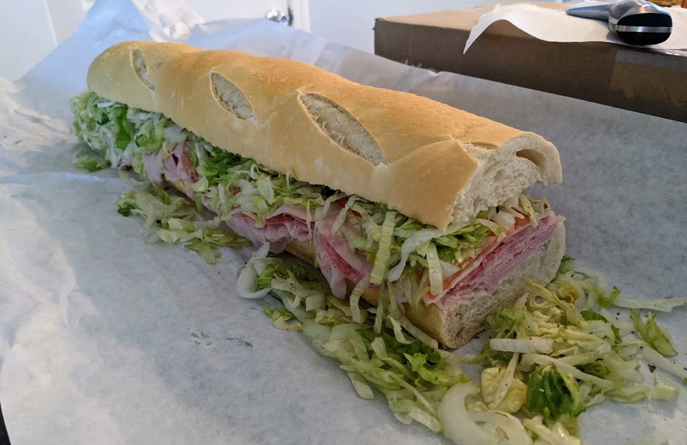Large Jersey Shore deli sandwich on a long roll with Italian meats, cheese, shredded lettuce, and onions