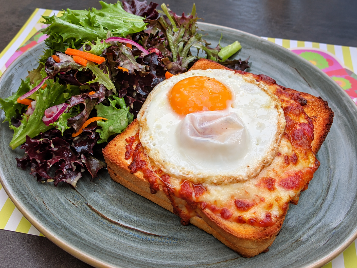 Croque madame with a fried egg, melted cheese, and salad
