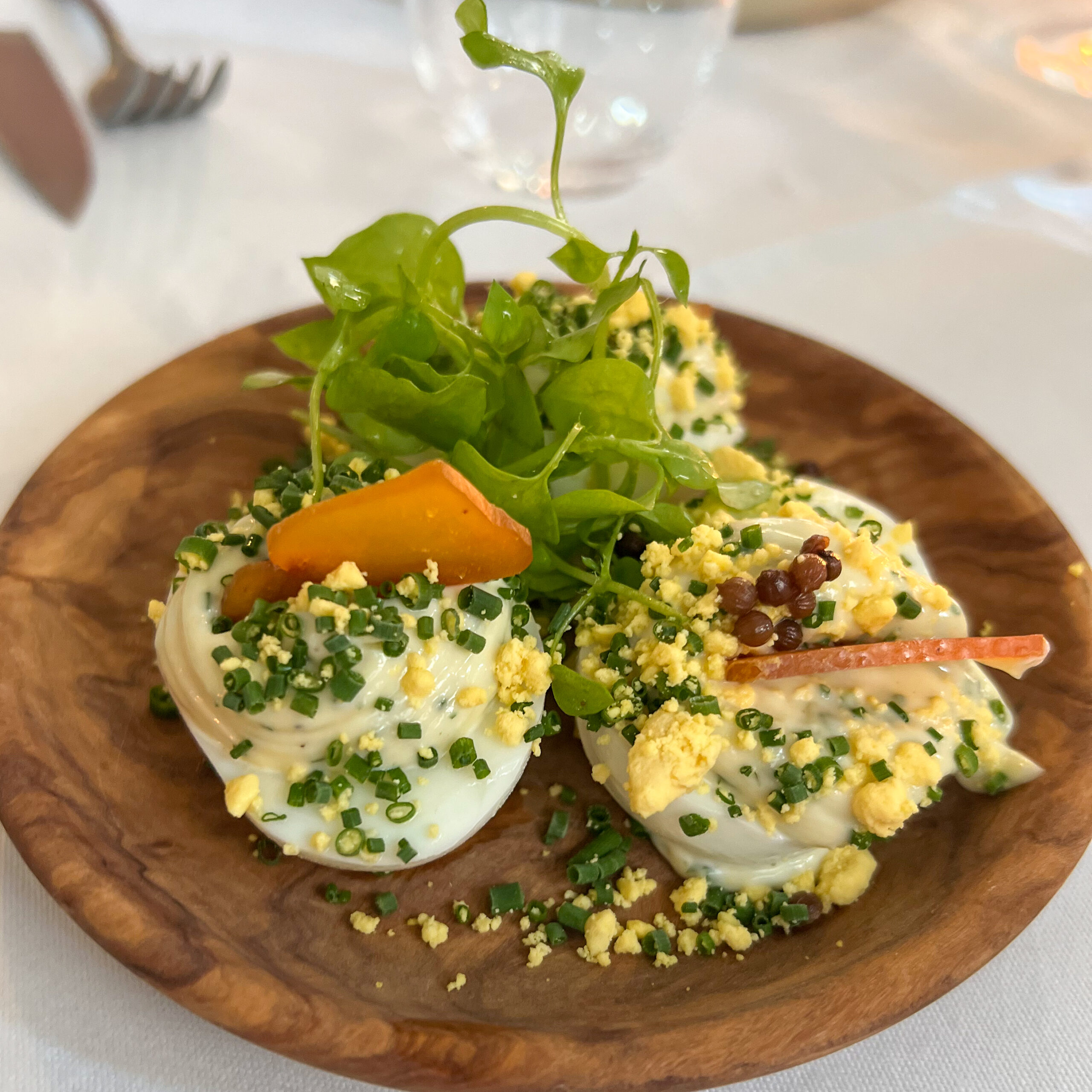 Œufs mayonnaise topped with chives, herbs, and vegetables on a wooden plate