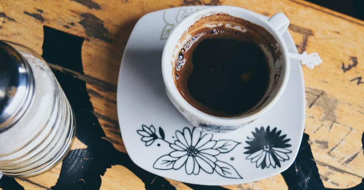 Cup of dark coffee served on a floral saucer on a wooden table