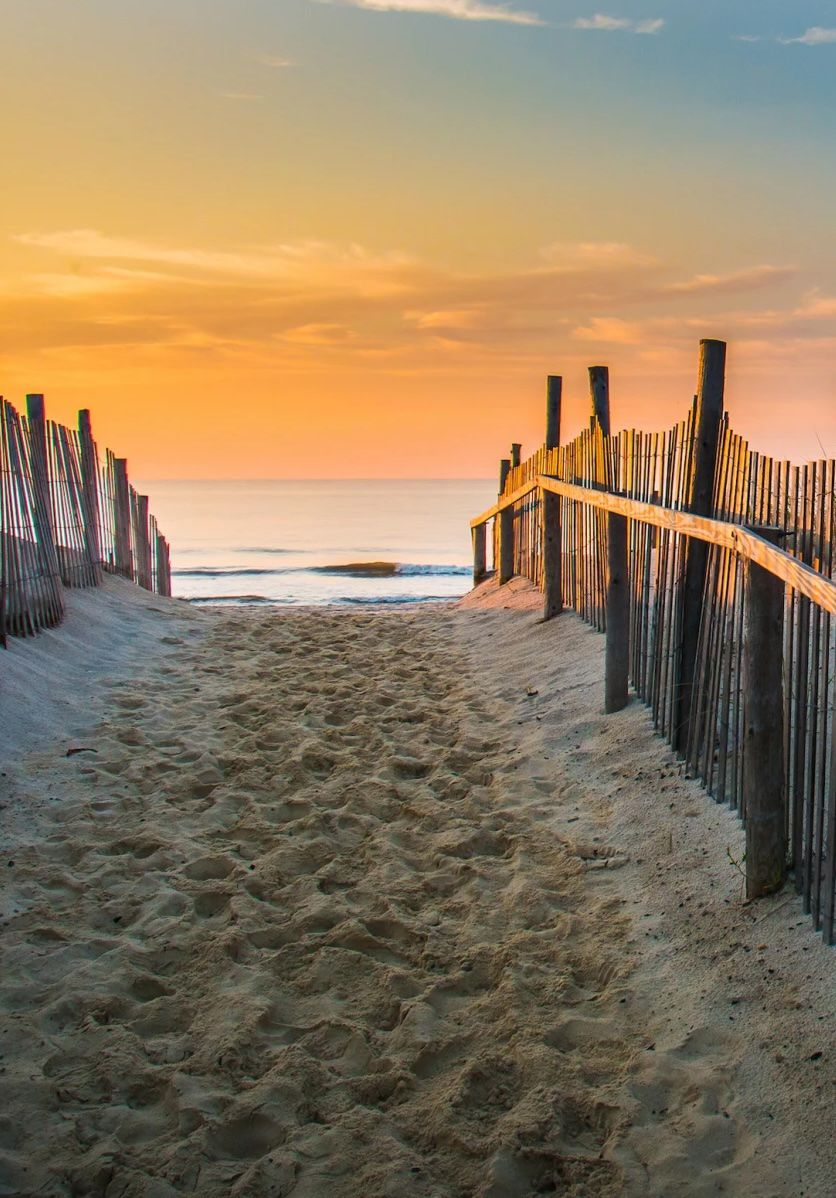 Sandy beach path between dune fences opening toward the ocean at sunset on the Jersey Shore